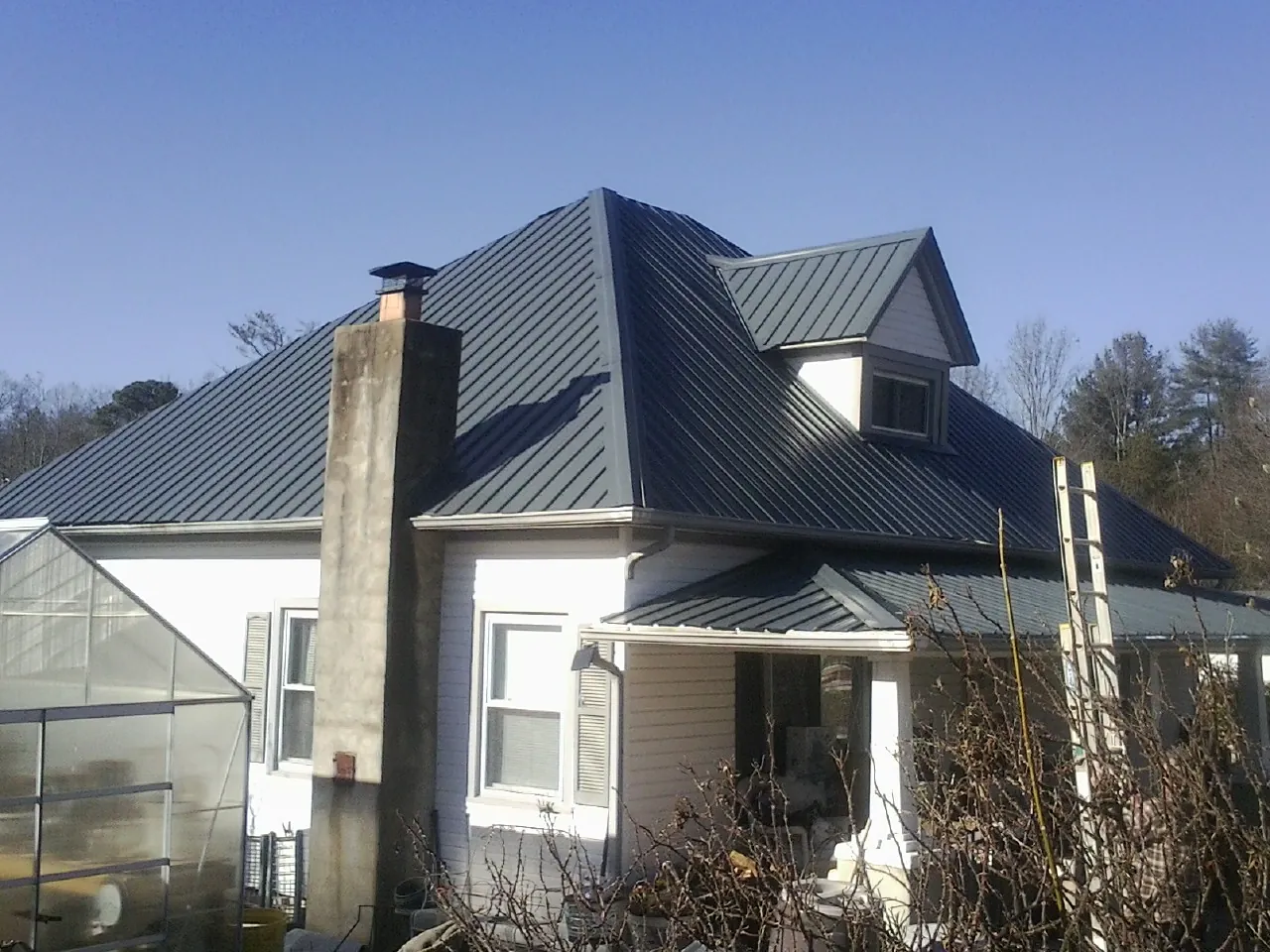 Dark blue standing seam metal roof on a white farmhouse with dormer — Slate & Tile Roof Repair by Roofing Brothers in Cedar Springs