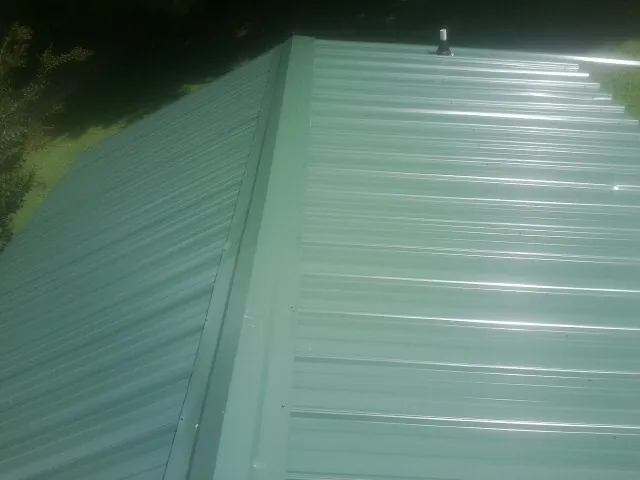 New green metal panels meeting at the ridge of a roof — Flat Roof Repair work by our crew in Cedar Springs