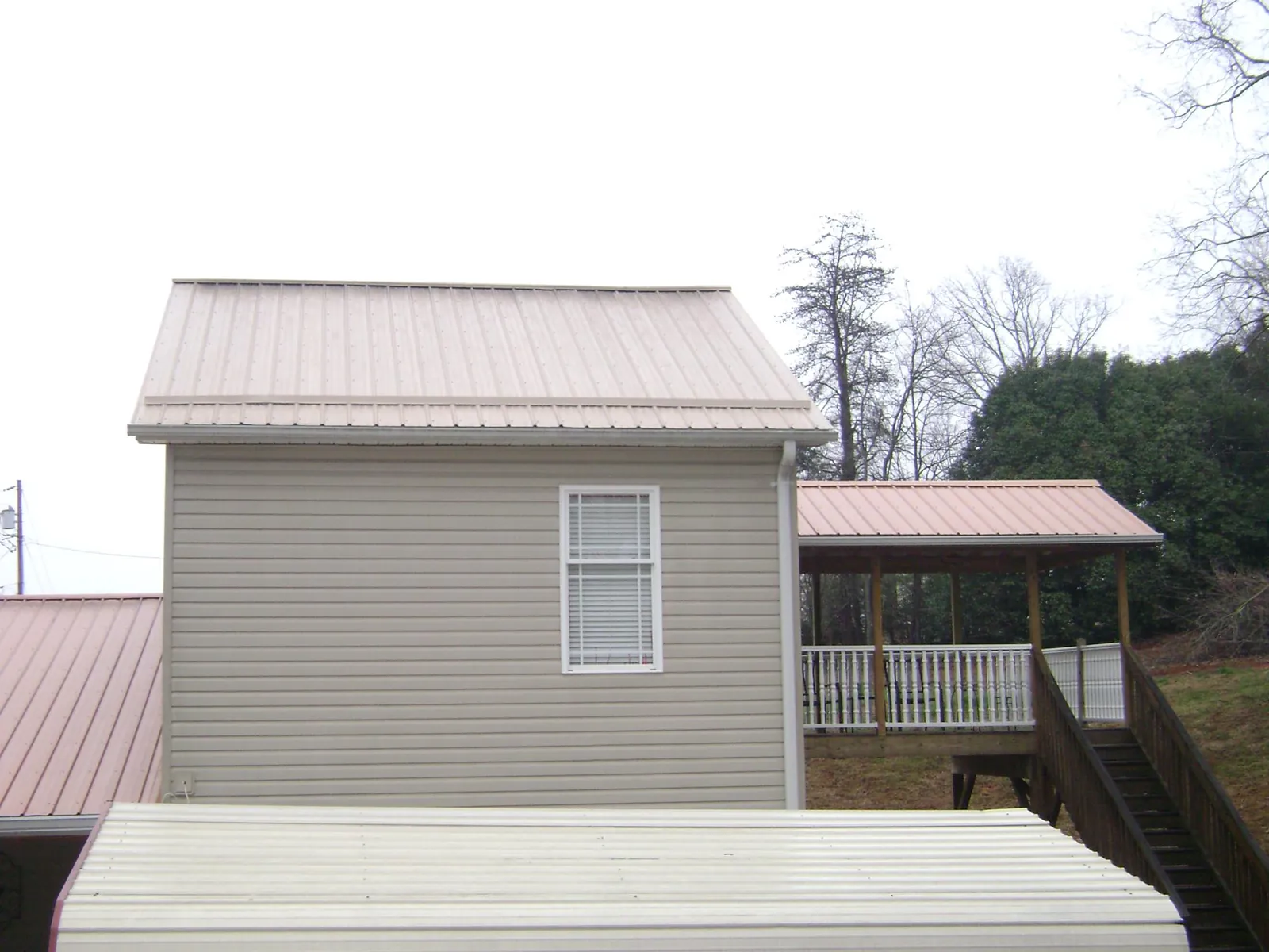 Tan metal roofs on a two story addition and attached porch, from a Roof Replacement job in Cedar Springs